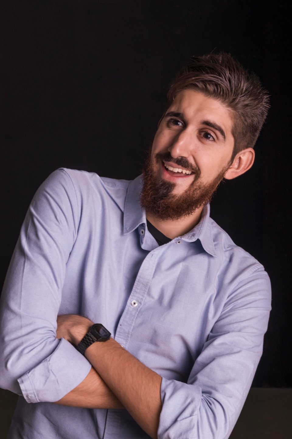 A man in a blue shirt smiles with arms crossed.