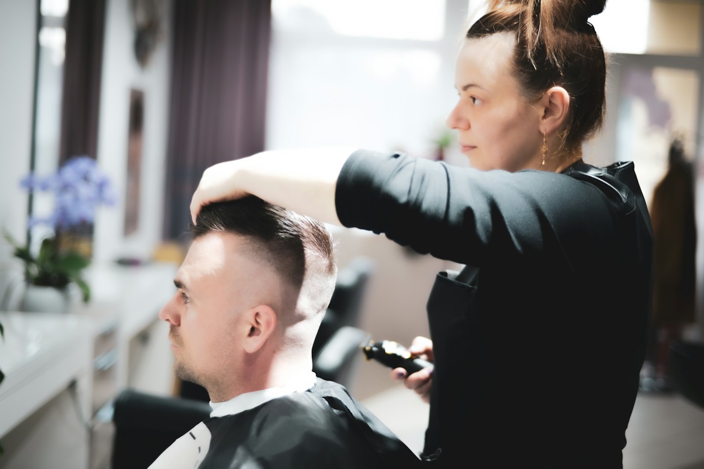Hairdresser trims customer's fade haircut with clippers.