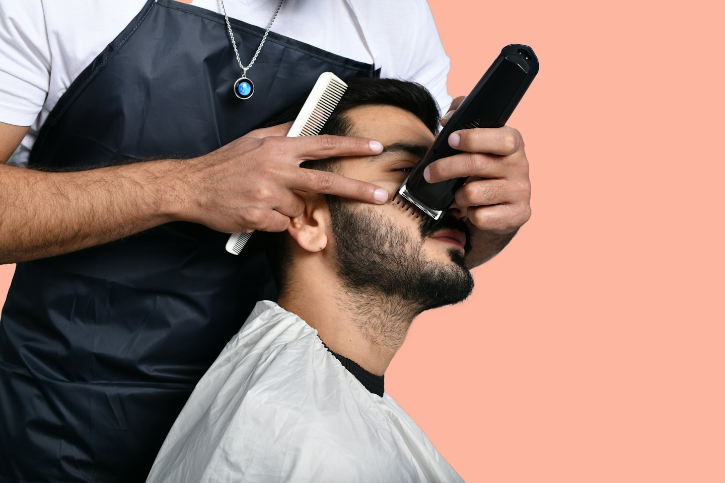 Barber uses an electric trimmer to groom a client's beard.