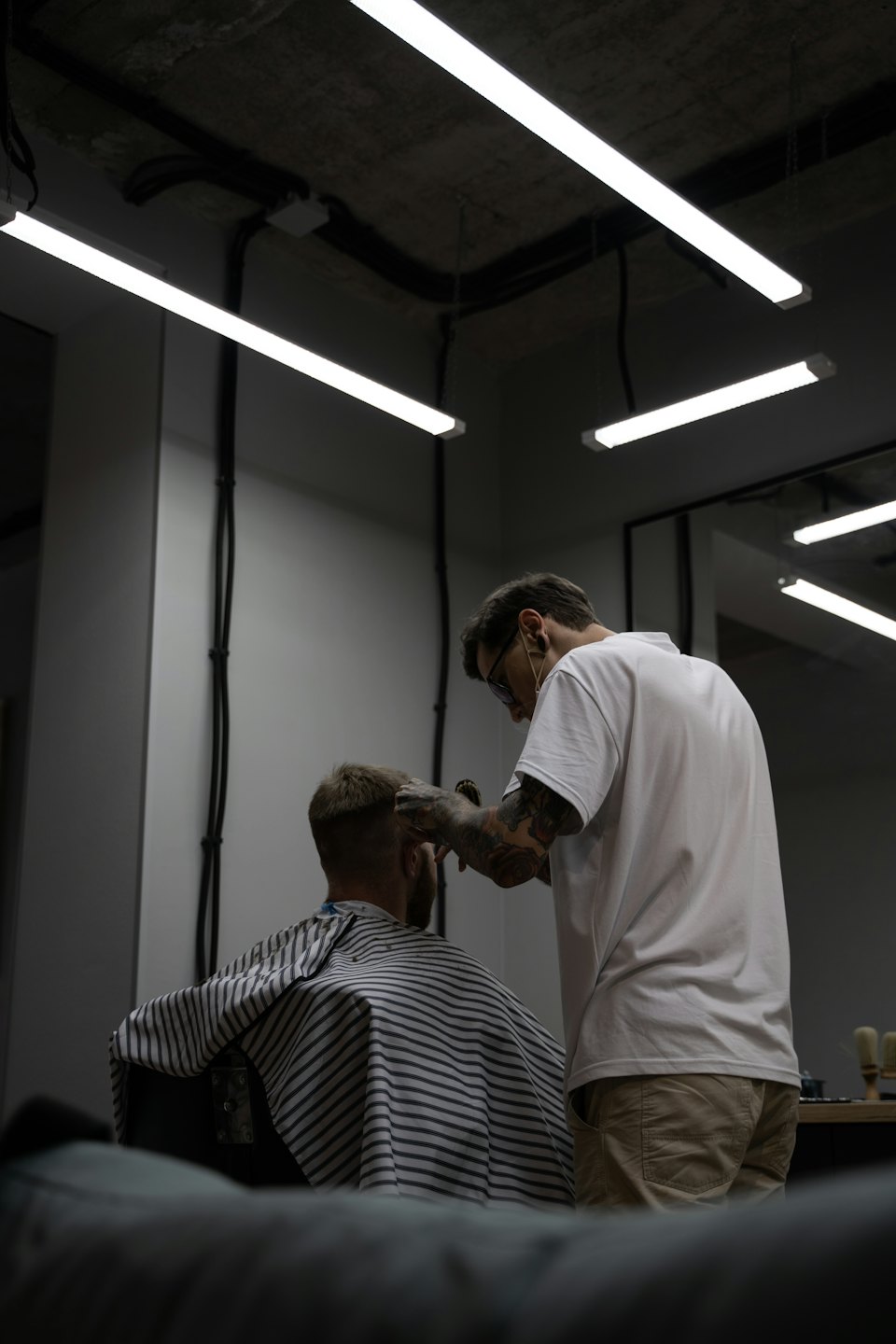 A barber with tattooed arms cuts a client's hair.
